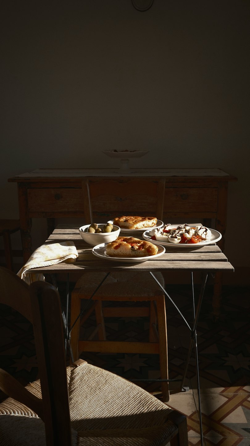 Des assiettes de focaccia, d'olives et de salade Caprese sont disposées sur une table rustique.